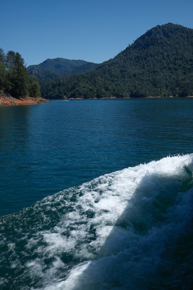 Boat wake diagonal across Shasta Lake with hills behind