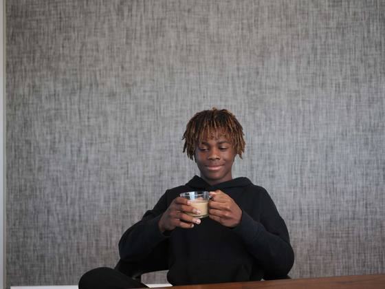 Boy holding a mug, seated low against a large textured grey wall