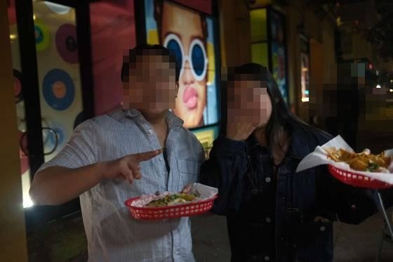 Two friends laughing with red baskets of food in front of a pop-art mural at night