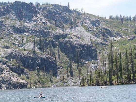 Tiny paddleboarder on an alpine lake beneath a massive talus wall