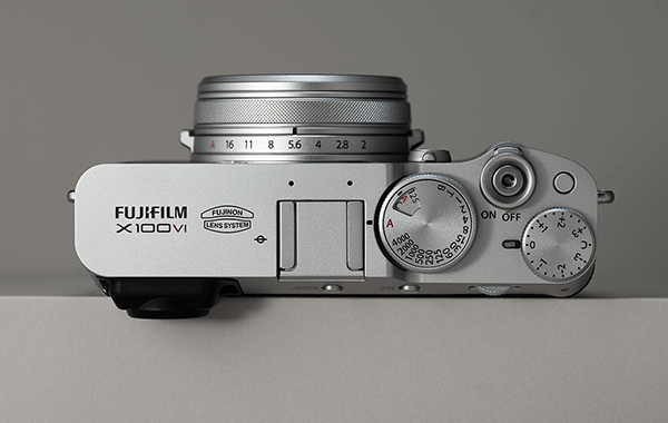 Official Fujifilm top view of the silver X100VI: aperture ring numerals, combined shutter-speed and ISO dial, and exposure compensation dial all legible
